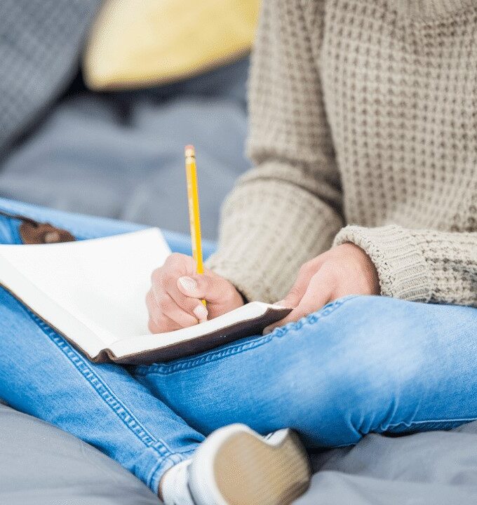writing-down-goals-in-a-notebook-young-woman-wearing-a-sweater-and-jeans